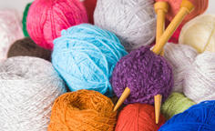 Closeup pile of colourful yarn balls, white, blue, pink, purple and brown with wooden knitting needles in middle